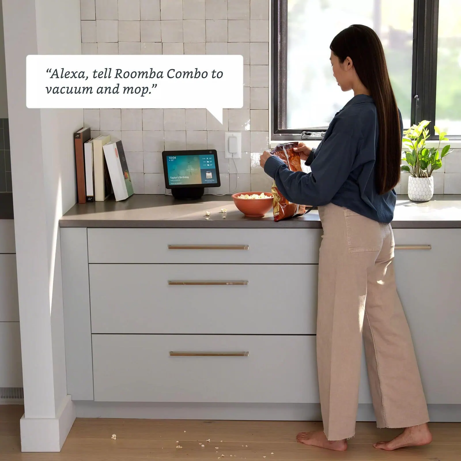 A person sending the Roomba&reg; 115 Combo robot to clean by voice through a smart speaker in the kitchen